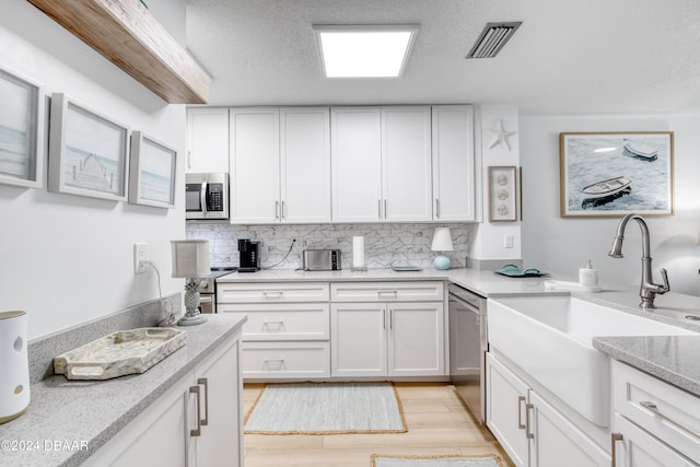 kitchen featuring stainless steel appliances, sink, tasteful backsplash, white cabinets, and light wood-type flooring