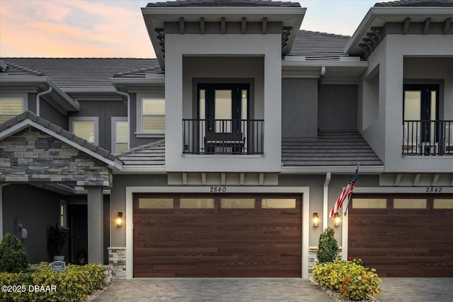 view of front of property featuring a garage, stone siding, a tile roof, decorative driveway, and stucco siding