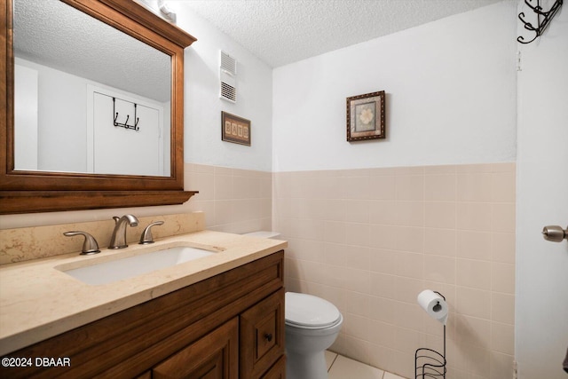 bathroom with a textured ceiling, vanity, tile patterned floors, toilet, and tile walls