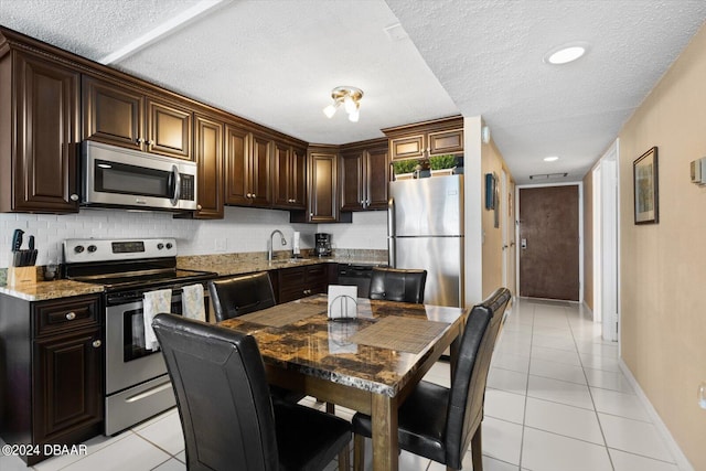 kitchen featuring light stone counters, light tile patterned flooring, stainless steel appliances, a textured ceiling, and dark brown cabinetry