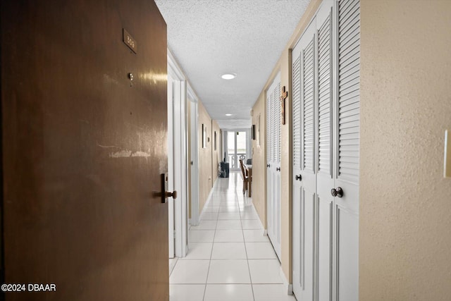 hall with a textured ceiling and light tile patterned floors