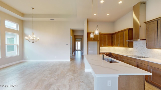 kitchen featuring black electric cooktop, a center island with sink, sink, light stone counters, and wall chimney exhaust hood