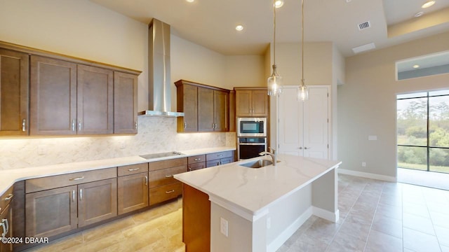 kitchen with stainless steel appliances, a center island with sink, light stone counters, tasteful backsplash, and wall chimney exhaust hood