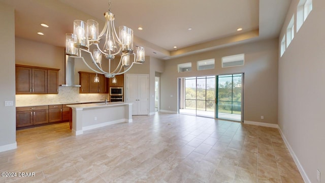 kitchen featuring a center island with sink, wall chimney exhaust hood, tasteful backsplash, pendant lighting, and appliances with stainless steel finishes