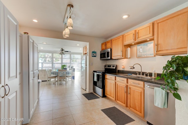 kitchen with light tile patterned floors, a sink, appliances with stainless steel finishes, dark countertops, and a ceiling fan