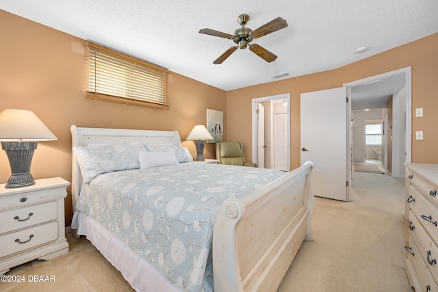 bedroom featuring ceiling fan, ensuite bath, a textured ceiling, and light colored carpet