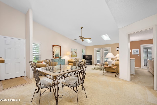 carpeted dining area with high vaulted ceiling, a skylight, french doors, and ceiling fan