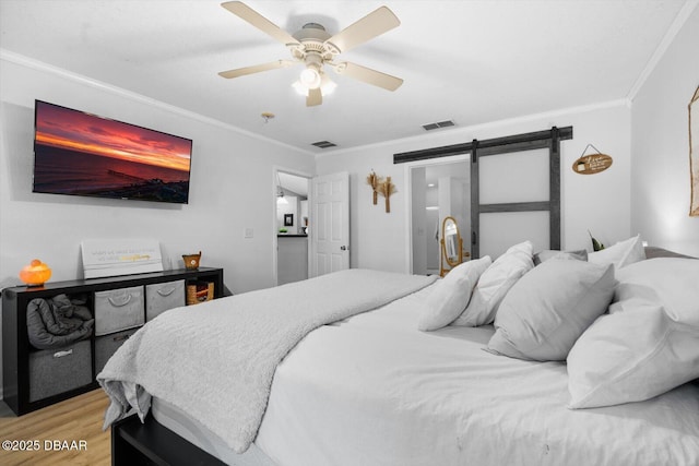 bedroom with a barn door, light hardwood / wood-style floors, ceiling fan, and crown molding