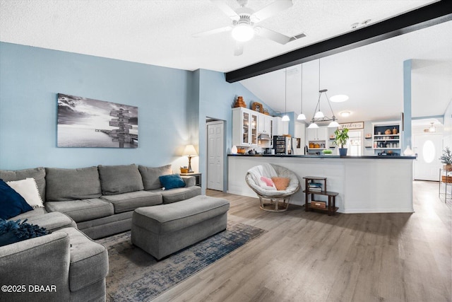 living room with a textured ceiling, lofted ceiling with beams, light hardwood / wood-style floors, and ceiling fan