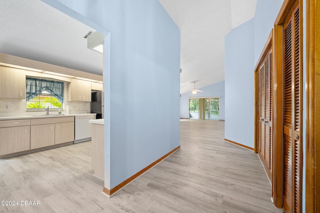 corridor featuring a textured ceiling, sink, light hardwood / wood-style flooring, and vaulted ceiling