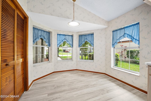 unfurnished dining area with a textured ceiling, vaulted ceiling, and light hardwood / wood-style flooring