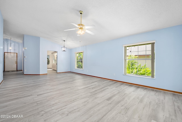 unfurnished room featuring a textured ceiling, ceiling fan with notable chandelier, a wealth of natural light, and light hardwood / wood-style floors