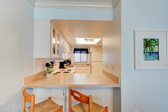 kitchen with white cabinetry, ornamental molding, white appliances, and a skylight