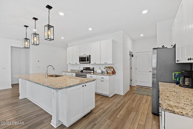 kitchen with sink, a kitchen island with sink, white cabinetry, light wood-type flooring, and appliances with stainless steel finishes