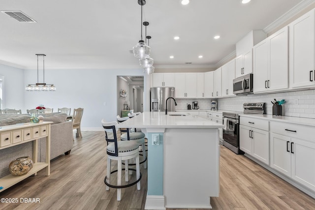 kitchen featuring a breakfast bar, visible vents, a sink, stainless steel appliances, and tasteful backsplash