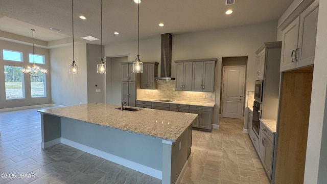 kitchen featuring wall chimney exhaust hood, light stone counters, a spacious island, pendant lighting, and appliances with stainless steel finishes