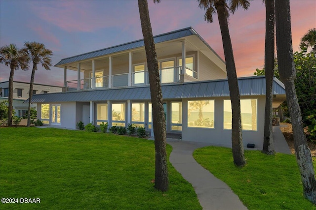 back house at dusk with a balcony and a yard