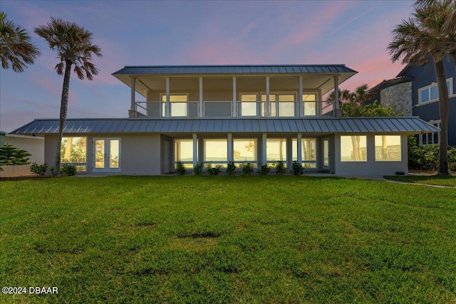 back house at dusk with a lawn and a balcony