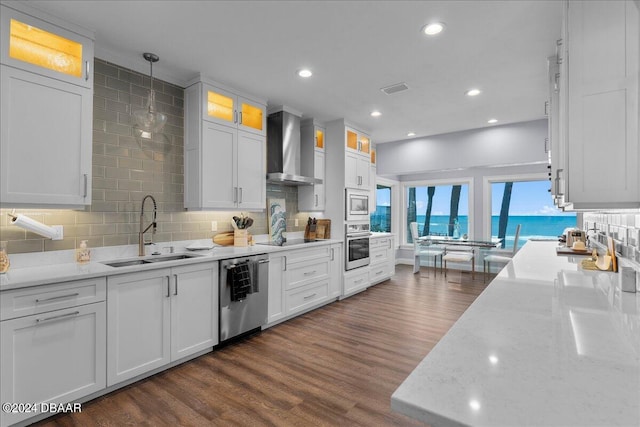 kitchen with stainless steel appliances, white cabinetry, sink, wall chimney range hood, and pendant lighting