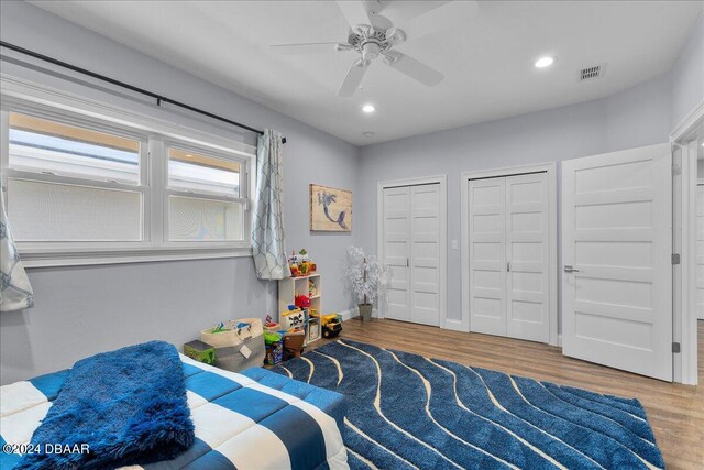 bedroom with hardwood / wood-style floors, ceiling fan, and two closets