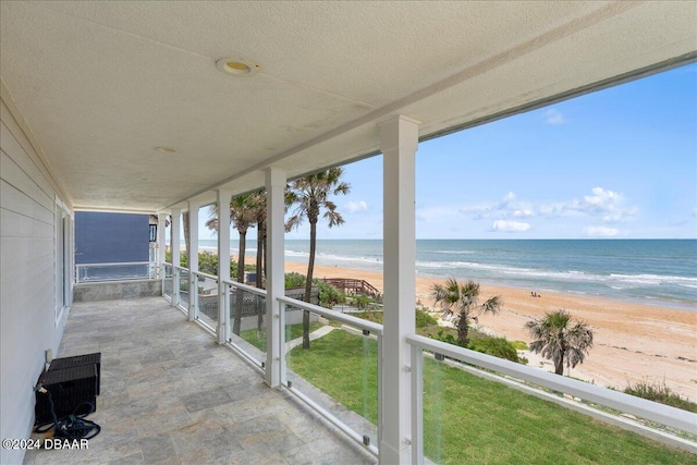 unfurnished sunroom featuring a view of the beach and a water view