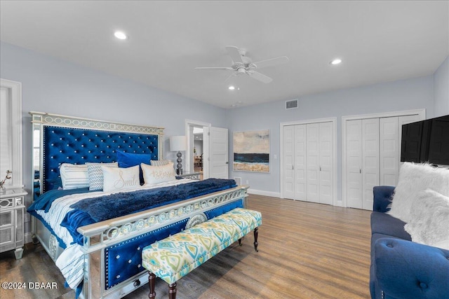 bedroom with hardwood / wood-style flooring, ceiling fan, and two closets