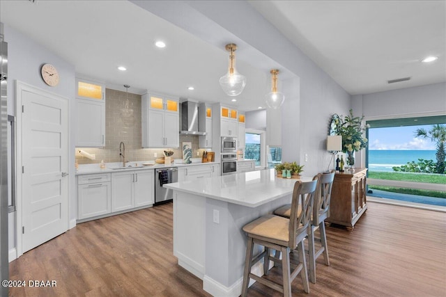 kitchen featuring stainless steel appliances, a water view, hardwood / wood-style flooring, wall chimney range hood, and white cabinetry