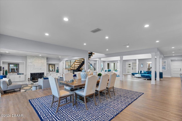 dining room featuring a stone fireplace, ornate columns, and light hardwood / wood-style floors