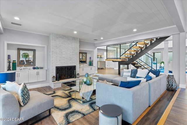 living room with a stone fireplace, ornamental molding, and hardwood / wood-style flooring