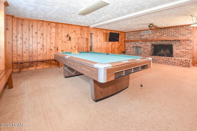 game room featuring pool table, a brick fireplace, a textured ceiling, wooden walls, and light colored carpet