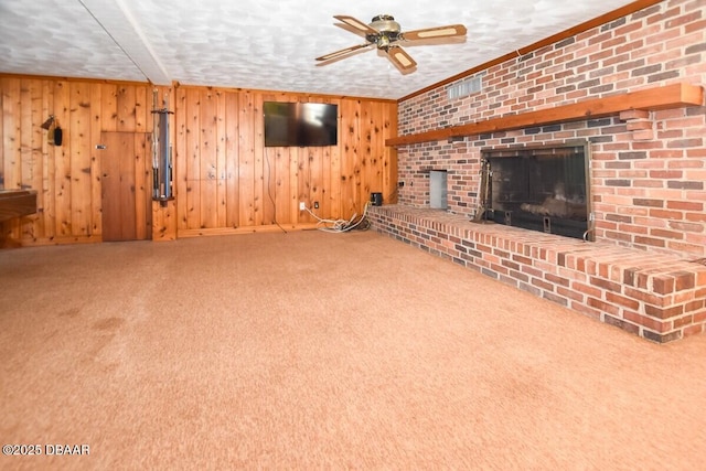 unfurnished living room featuring a brick fireplace, wooden walls, ceiling fan, and carpet flooring