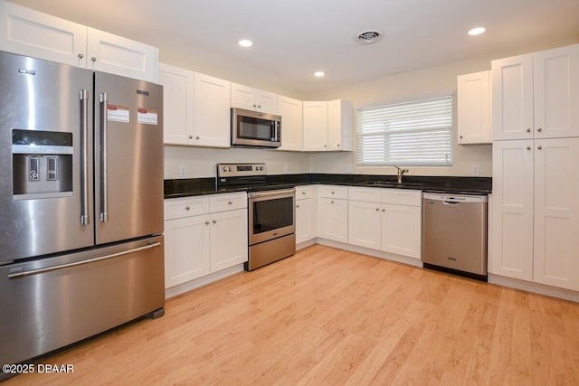 kitchen featuring appliances with stainless steel finishes, sink, white cabinets, and light wood-type flooring