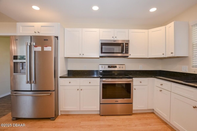 kitchen featuring appliances with stainless steel finishes, white cabinetry, sink, dark stone counters, and light wood-type flooring