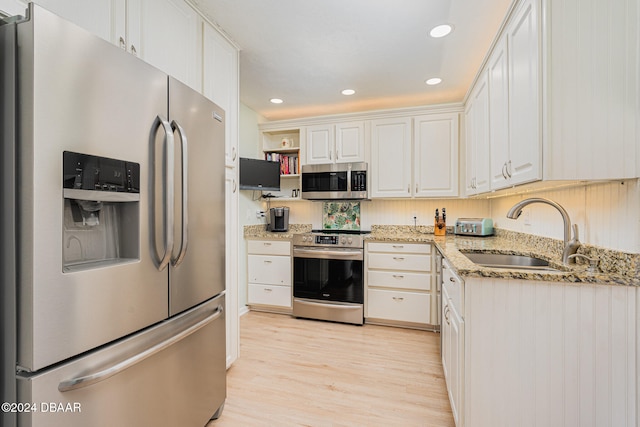 kitchen featuring white cabinetry, sink, light stone counters, light hardwood / wood-style flooring, and appliances with stainless steel finishes