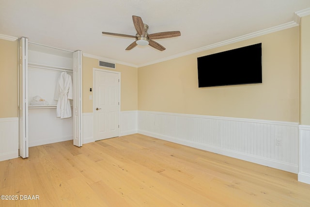 unfurnished bedroom featuring ornamental molding, wood finished floors, visible vents, and wainscoting