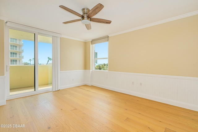 empty room featuring ornamental molding, a ceiling fan, light wood-type flooring, and wainscoting