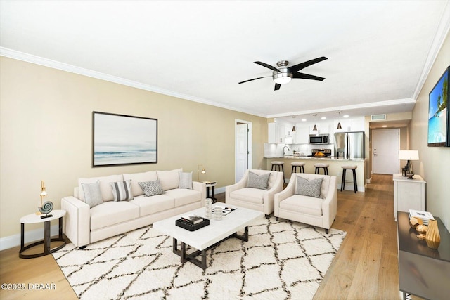 living area featuring visible vents, light wood-style flooring, crown molding, baseboards, and ceiling fan