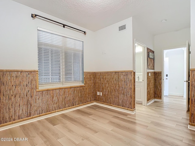 unfurnished room with light hardwood / wood-style floors, a textured ceiling, and wood walls