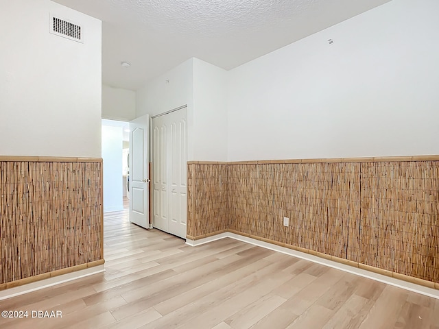 empty room with wooden walls, light hardwood / wood-style flooring, and a textured ceiling