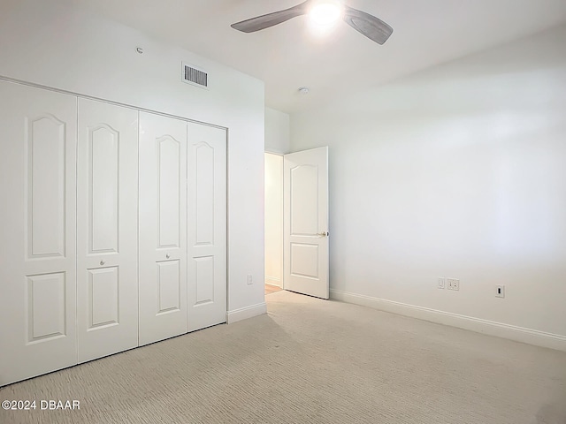 unfurnished bedroom with light colored carpet, a closet, and ceiling fan