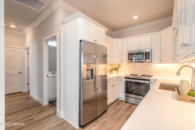 kitchen featuring light wood-type flooring, tasteful backsplash, stainless steel appliances, sink, and white cabinetry