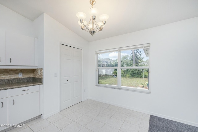 unfurnished dining area featuring baseboards, lofted ceiling, light tile patterned flooring, and a notable chandelier