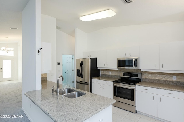 kitchen featuring a peninsula, a chandelier, tasteful backsplash, a sink, and stainless steel appliances