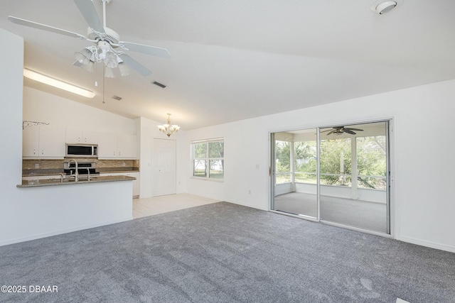unfurnished living room with visible vents, light colored carpet, a sink, ceiling fan with notable chandelier, and lofted ceiling
