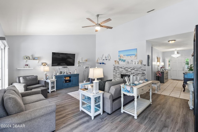 living area with ceiling fan with notable chandelier, a tile fireplace, visible vents, and wood finished floors