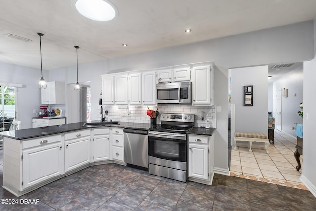 kitchen featuring stainless steel appliances, a peninsula, a sink, decorative backsplash, and dark countertops