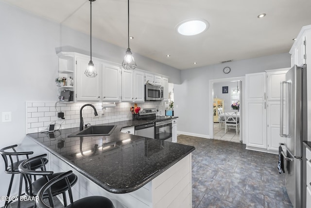 kitchen with white cabinets, appliances with stainless steel finishes, a peninsula, a sink, and backsplash