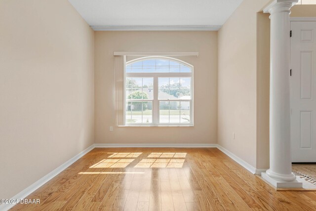 spare room featuring light hardwood / wood-style floors and ornate columns