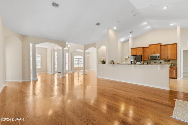 living room featuring light wood-type flooring, decorative columns, and high vaulted ceiling