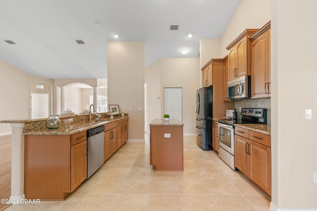 kitchen with kitchen peninsula, stainless steel appliances, light stone countertops, and sink